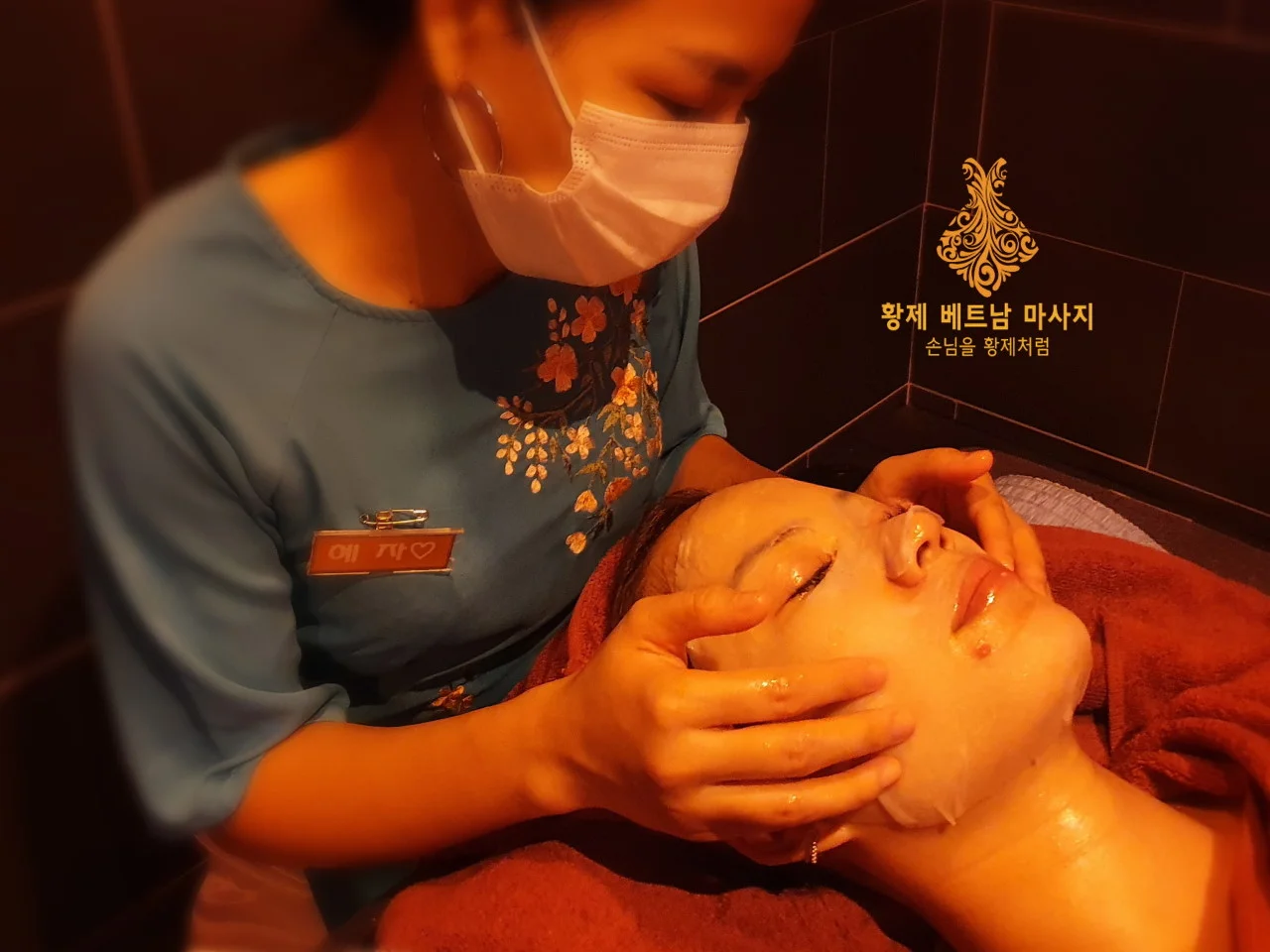 고객의 얼굴에 마스크 팩을 얹고 정성스럽게 페이셜 마사지를 진행하는 모습